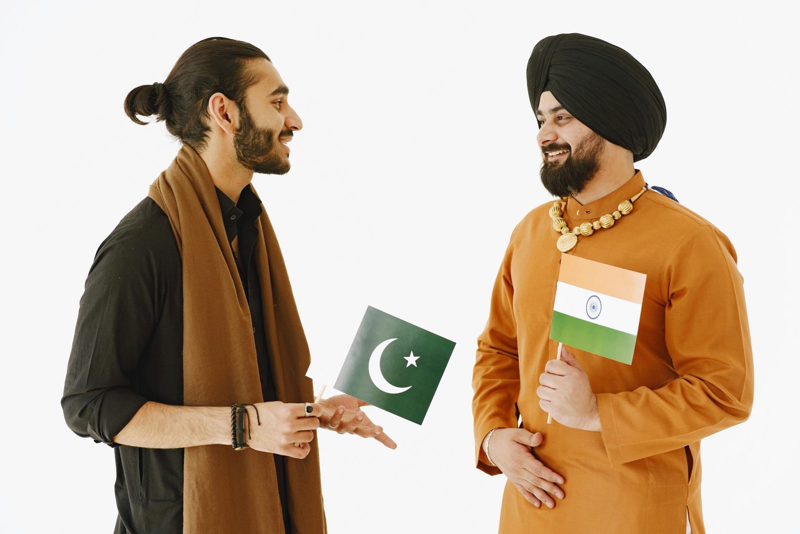 Two men, holding Indian and Pakistani flags, engage in friendly conversation.